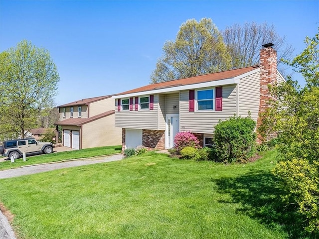 bi-level home featuring a garage, a chimney, driveway, and a front lawn