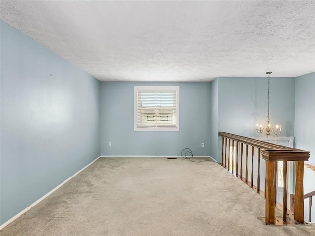 carpeted empty room featuring a textured ceiling, a chandelier, baseboards, and visible vents