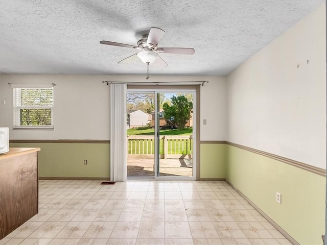 unfurnished room with baseboards, a textured ceiling, ceiling fan, and a wealth of natural light