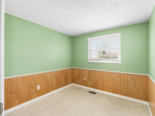 spare room with visible vents, carpet, wainscoting, and wooden walls