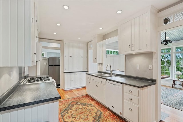 kitchen featuring dark countertops, white appliances, ceiling fan, light wood-type flooring, and a sink