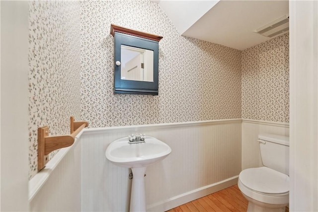 bathroom featuring wainscoting, toilet, wallpapered walls, wood finished floors, and visible vents