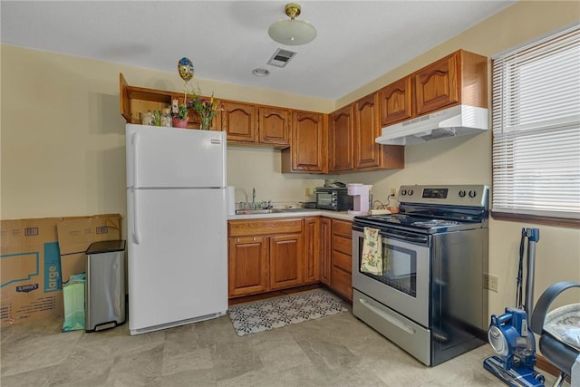 kitchen featuring a sink, stainless steel range with electric stovetop, freestanding refrigerator, under cabinet range hood, and visible vents