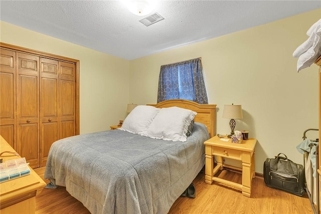 bedroom with a textured ceiling, visible vents, light wood finished floors, and a closet