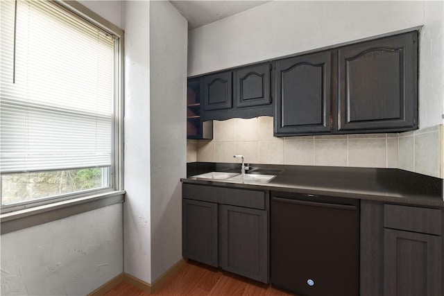 kitchen with dark countertops, a sink, light wood finished floors, decorative backsplash, and dishwashing machine