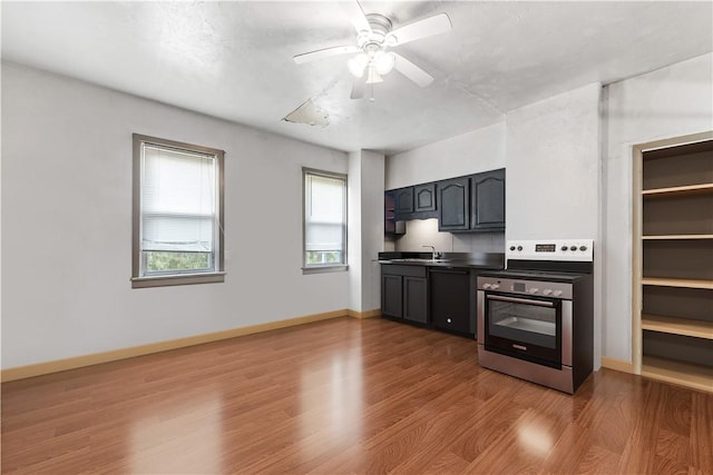 kitchen featuring dark countertops, a sink, stainless steel range with electric stovetop, a ceiling fan, and wood finished floors