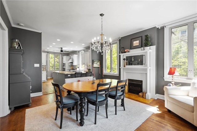 dining room with crown molding, a notable chandelier, light wood-style floors, a fireplace, and baseboards