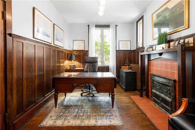 office area with wooden walls, wainscoting, dark wood-style flooring, and a tile fireplace
