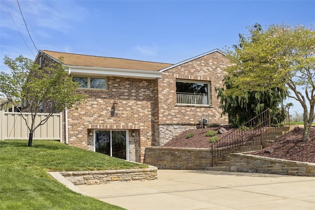 rear view of property featuring fence, brick siding, a shingled roof, stairs, and a yard