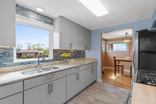 kitchen featuring light wood-style floors, tasteful backsplash, a sink, gray cabinetry, and stainless steel appliances