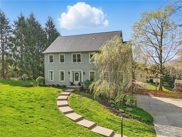 colonial home featuring fence, driveway, roof with shingles, and a front lawn