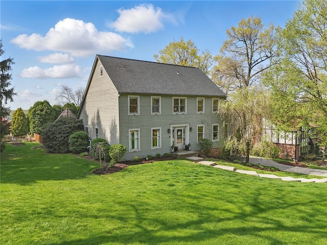 colonial inspired home featuring roof with shingles and a front yard