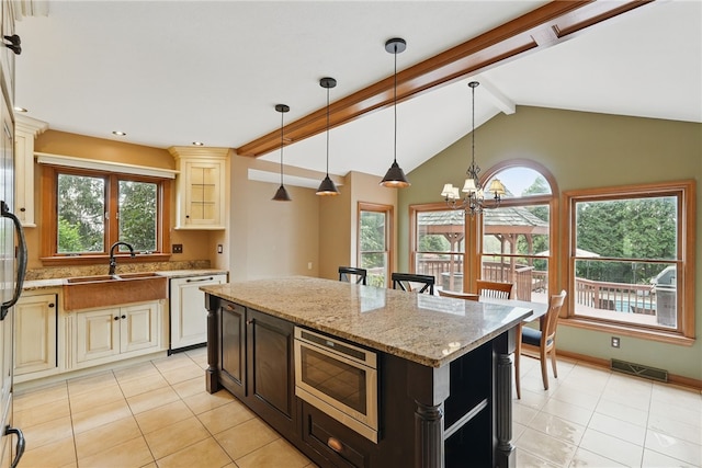 kitchen with dishwasher, a sink, stainless steel microwave, light tile patterned flooring, and cream cabinetry
