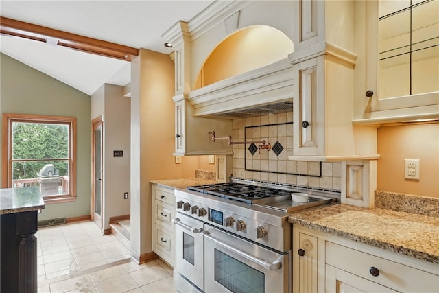 kitchen with decorative backsplash, range with two ovens, cream cabinets, lofted ceiling, and custom range hood