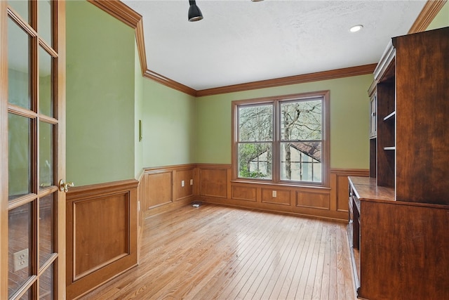 unfurnished office featuring crown molding, a wainscoted wall, and light wood-style flooring