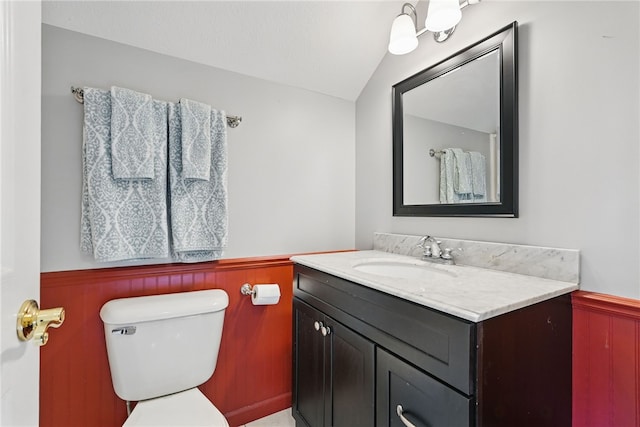 bathroom with vaulted ceiling, vanity, wainscoting, and toilet