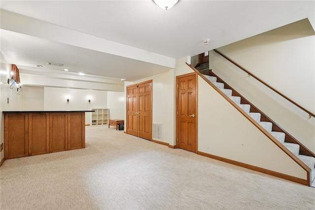 finished basement with baseboards, visible vents, light carpet, and stairway
