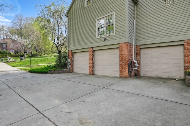view of side of home featuring a yard, brick siding, driveway, and a garage