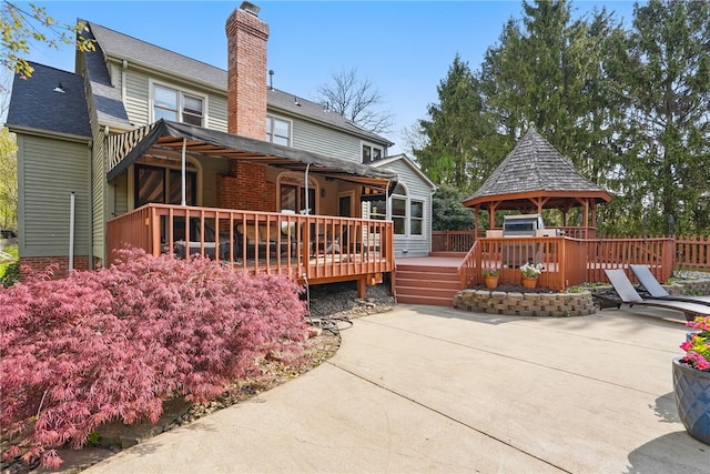 rear view of house featuring a chimney, a wooden deck, a patio area, a gazebo, and fence