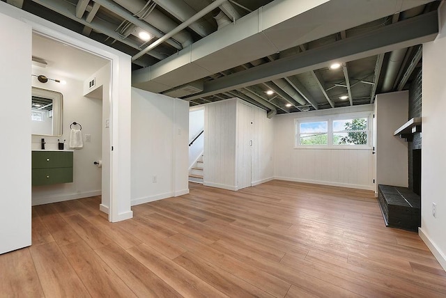 basement with baseboards, stairs, light wood-style flooring, and visible vents