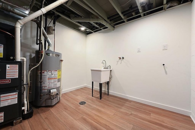 finished basement with baseboards, heating unit, water heater, and wood finished floors