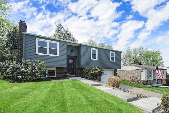 bi-level home featuring a chimney, an attached garage, brick siding, and a front yard