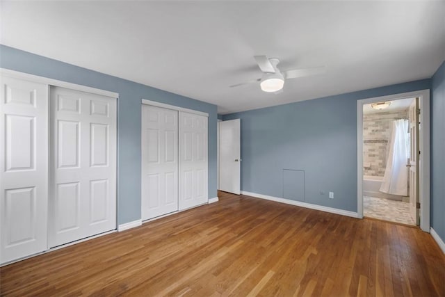unfurnished bedroom with a ceiling fan, wood finished floors, baseboards, multiple closets, and ensuite bathroom