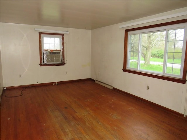 spare room featuring wood-type flooring, a baseboard heating unit, and a healthy amount of sunlight
