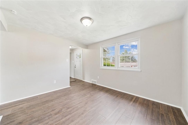 spare room with baseboards, wood finished floors, and visible vents