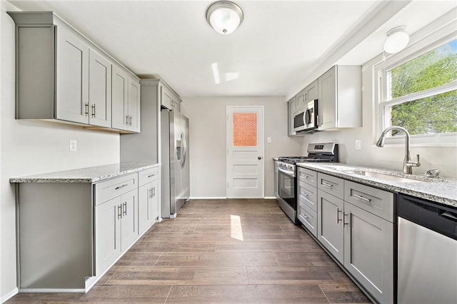 kitchen with gray cabinetry, appliances with stainless steel finishes, a sink, and light stone counters