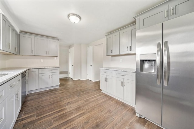 kitchen featuring gray cabinetry, appliances with stainless steel finishes, light stone countertops, and dark wood-style flooring