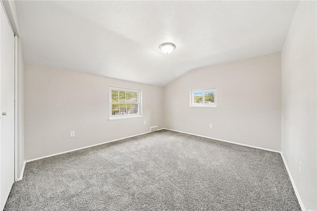 carpeted empty room featuring baseboards, visible vents, and lofted ceiling