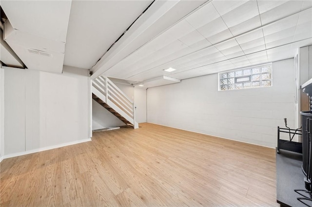 basement featuring light wood-type flooring, concrete block wall, and stairway