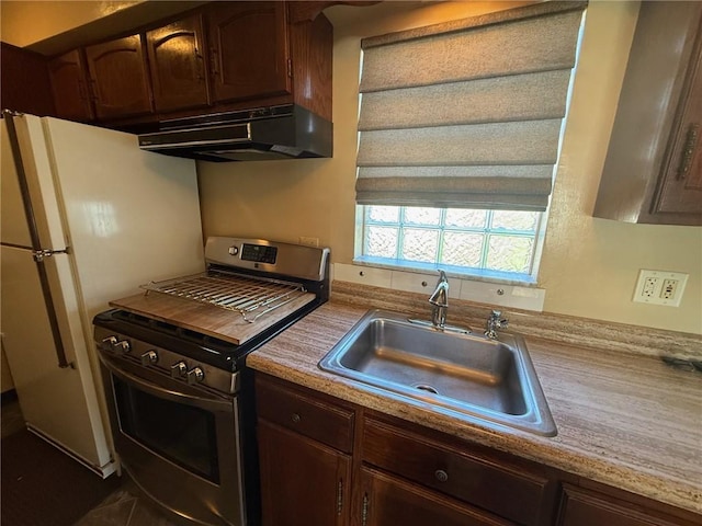 kitchen with a sink, under cabinet range hood, gas stove, and light countertops