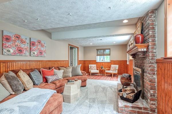 carpeted living area featuring wooden walls, wainscoting, a textured ceiling, and a brick fireplace