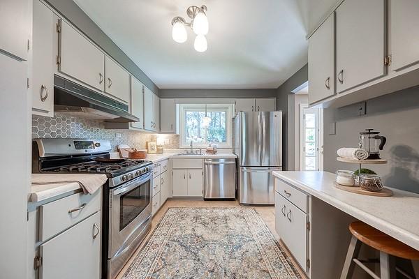 kitchen featuring backsplash, appliances with stainless steel finishes, a sink, light countertops, and under cabinet range hood