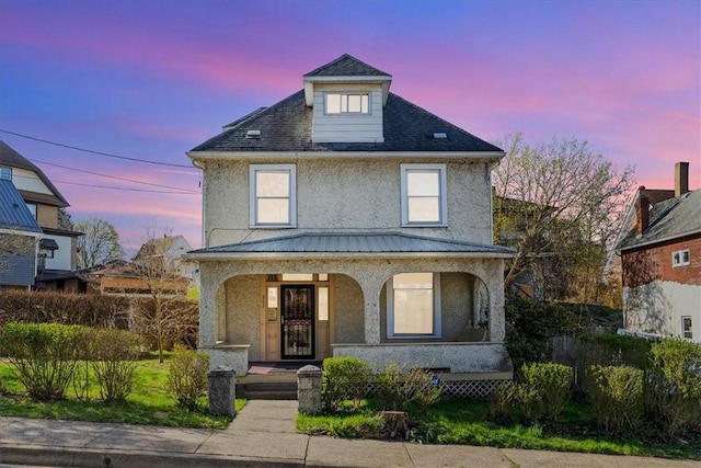 traditional style home featuring stucco siding, covered porch, and metal roof