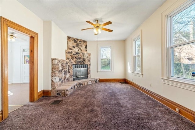 unfurnished living room with baseboards, ceiling fan, carpet flooring, and a stone fireplace