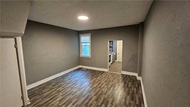 empty room featuring dark wood-style flooring, a textured wall, and baseboards