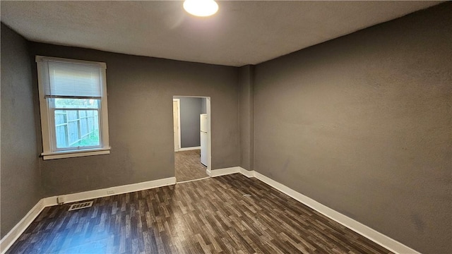 unfurnished room featuring baseboards, visible vents, and dark wood-style floors