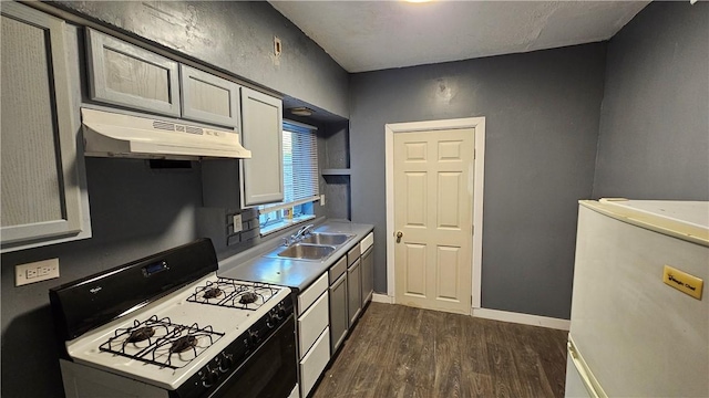 kitchen featuring gas range, a sink, baseboards, under cabinet range hood, and dark wood-type flooring