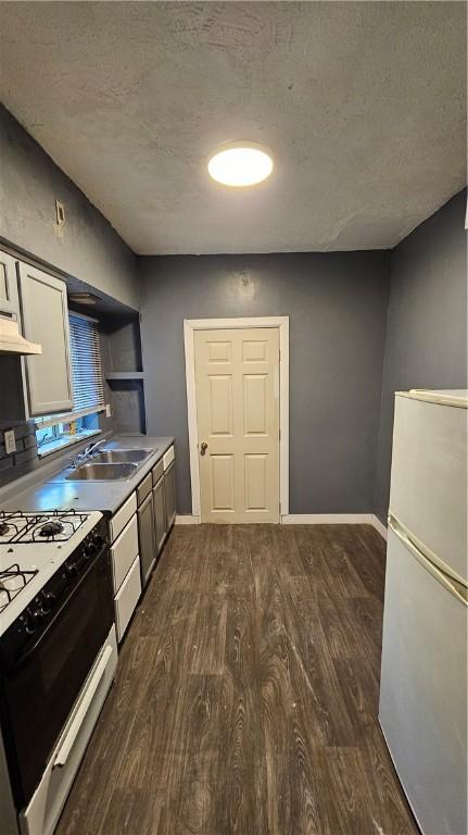 kitchen with dark wood-type flooring, a sink, freestanding refrigerator, and gas range