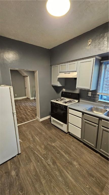 kitchen featuring a sink, white appliances, baseboards, under cabinet range hood, and dark wood-style floors