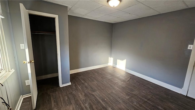 unfurnished bedroom with a paneled ceiling, baseboards, wood finished floors, and a closet