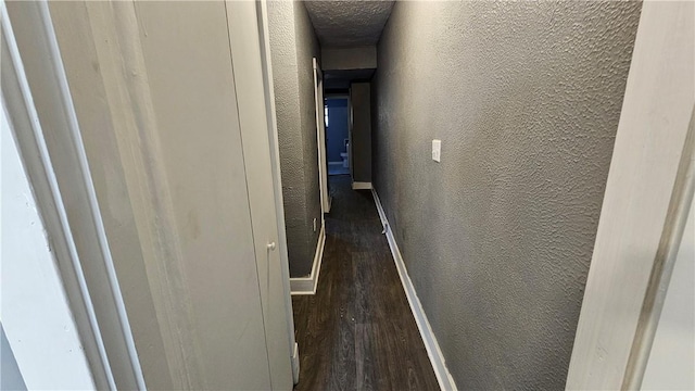hallway featuring baseboards, a textured wall, and wood finished floors