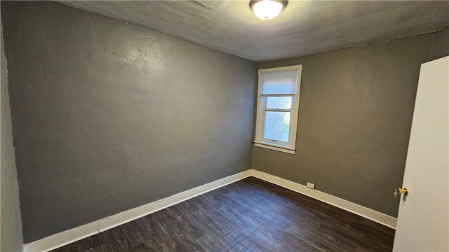 spare room with baseboards and dark wood-type flooring