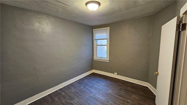 spare room featuring baseboards and dark wood finished floors