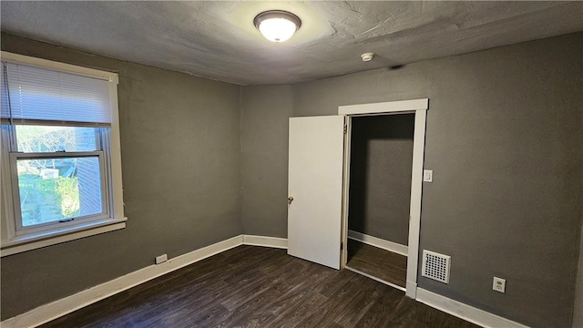 unfurnished bedroom featuring visible vents, dark wood-style flooring, and baseboards