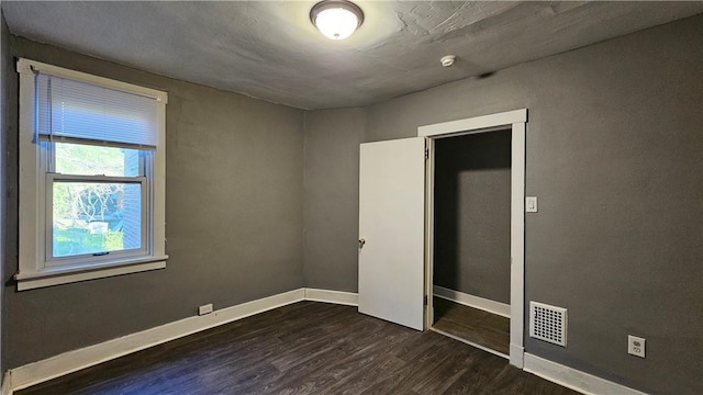unfurnished bedroom featuring dark wood-style flooring, baseboards, and visible vents