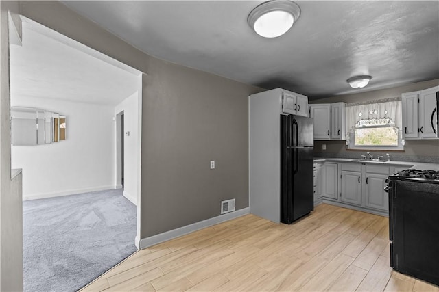 kitchen featuring a sink, light wood-style floors, black appliances, and visible vents